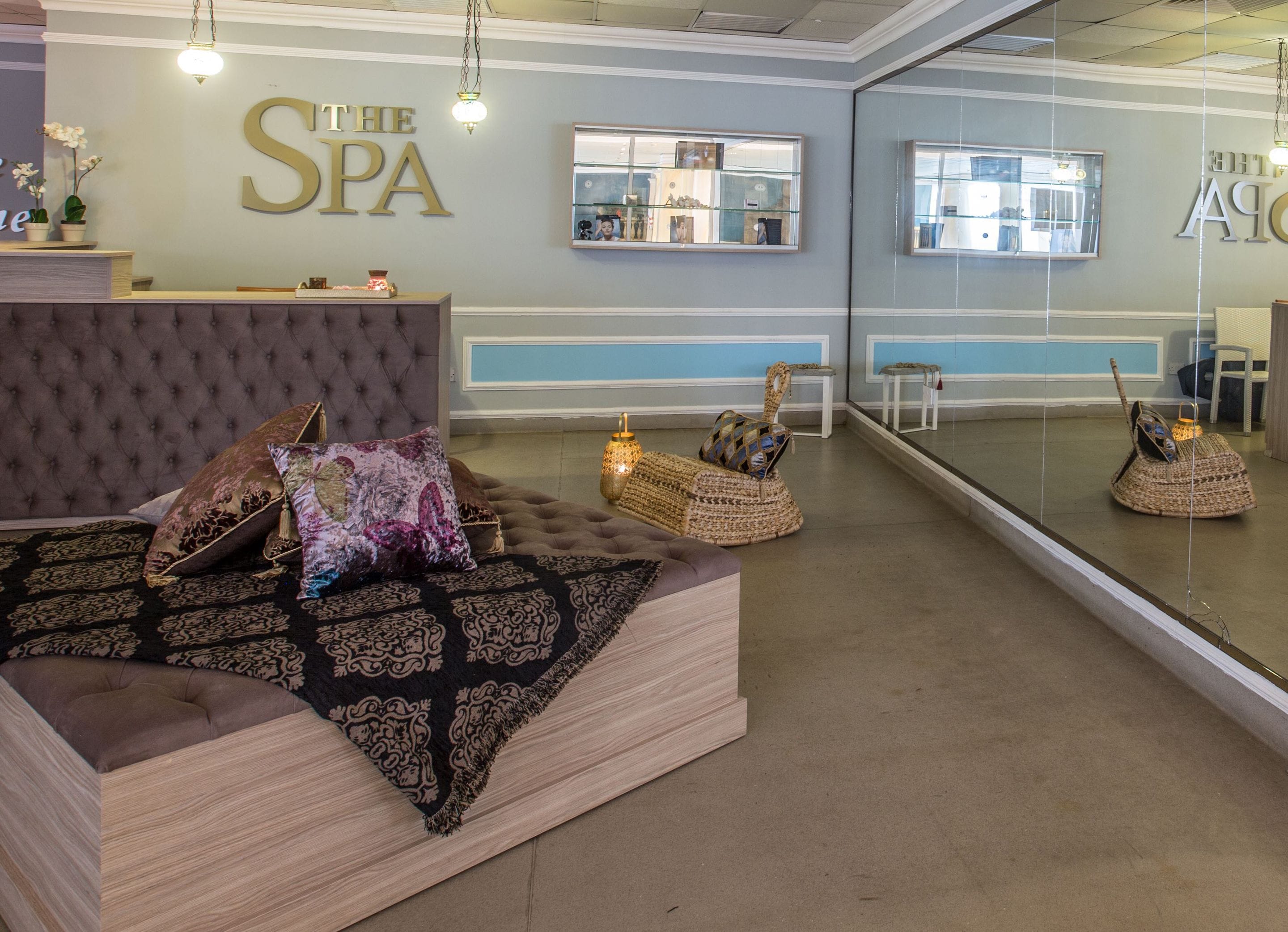 Zona de recepción de un spa, con un espejo grande, un mostrador y un área de estar con cojines estampados.