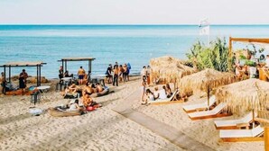 Ein Strand mit strohgedeckten Hütten und Liegestühlen.