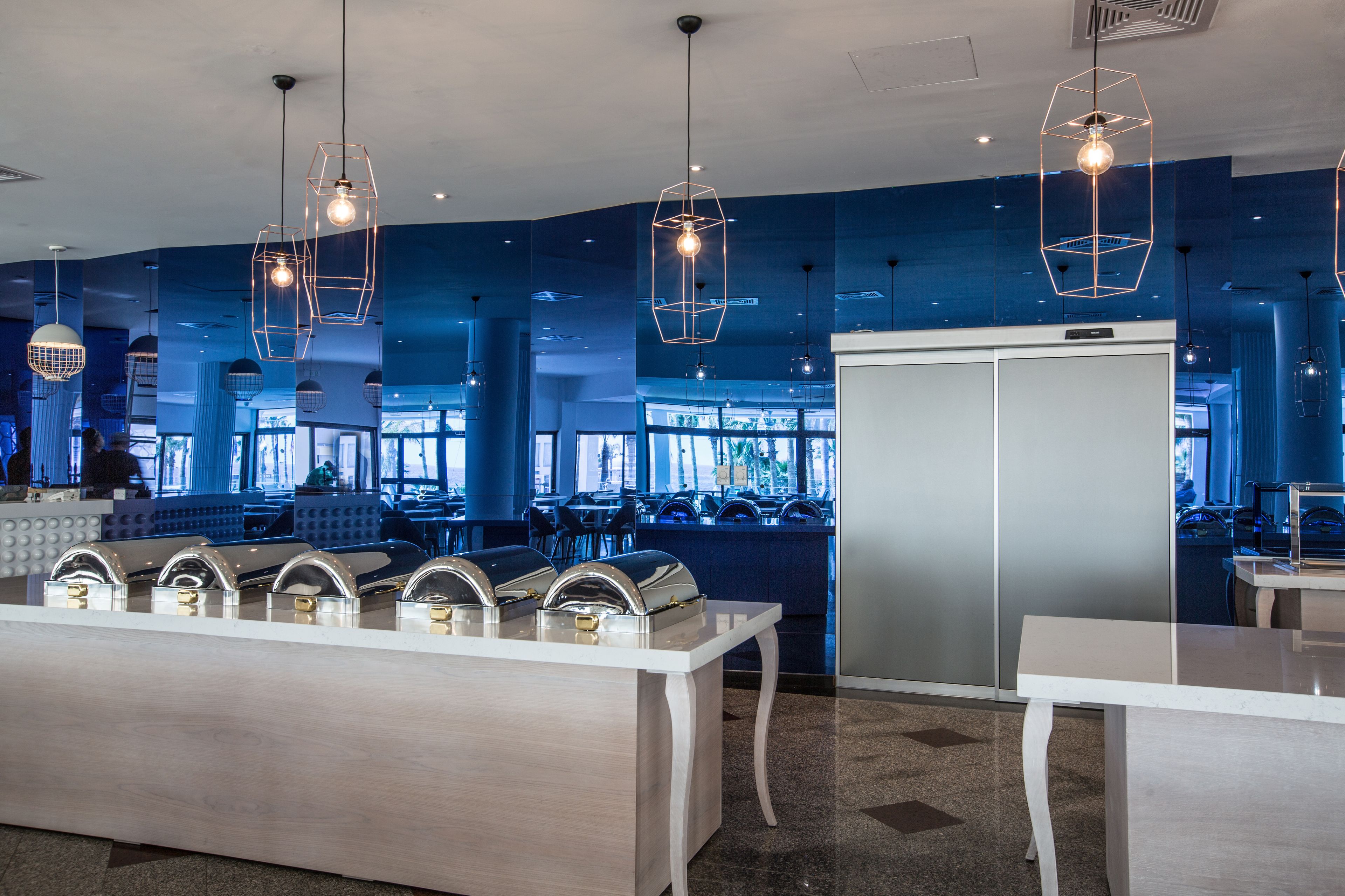 A modern restaurant interior with a blue color scheme, contemporary lighting fixtures, and a buffet setup.