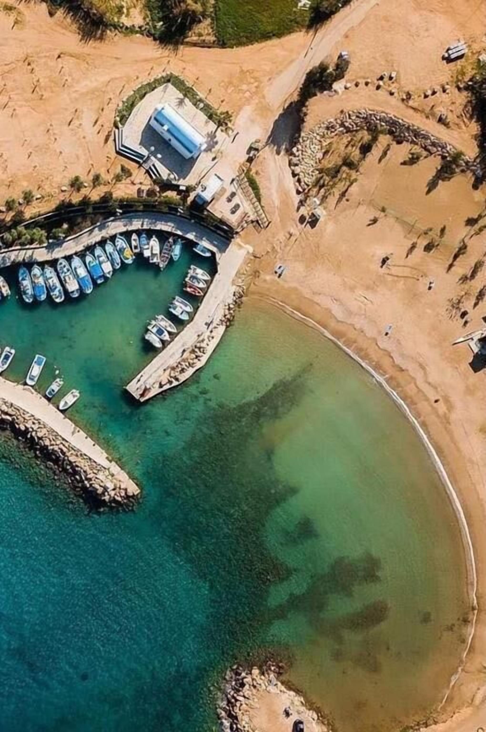 An aerial view of a coastal area with a circular dock, boats, and a small building.