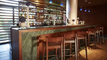 Una zona de bar con mostrador de mármol, taburetes de madera y una pared llena de botellas de licores.