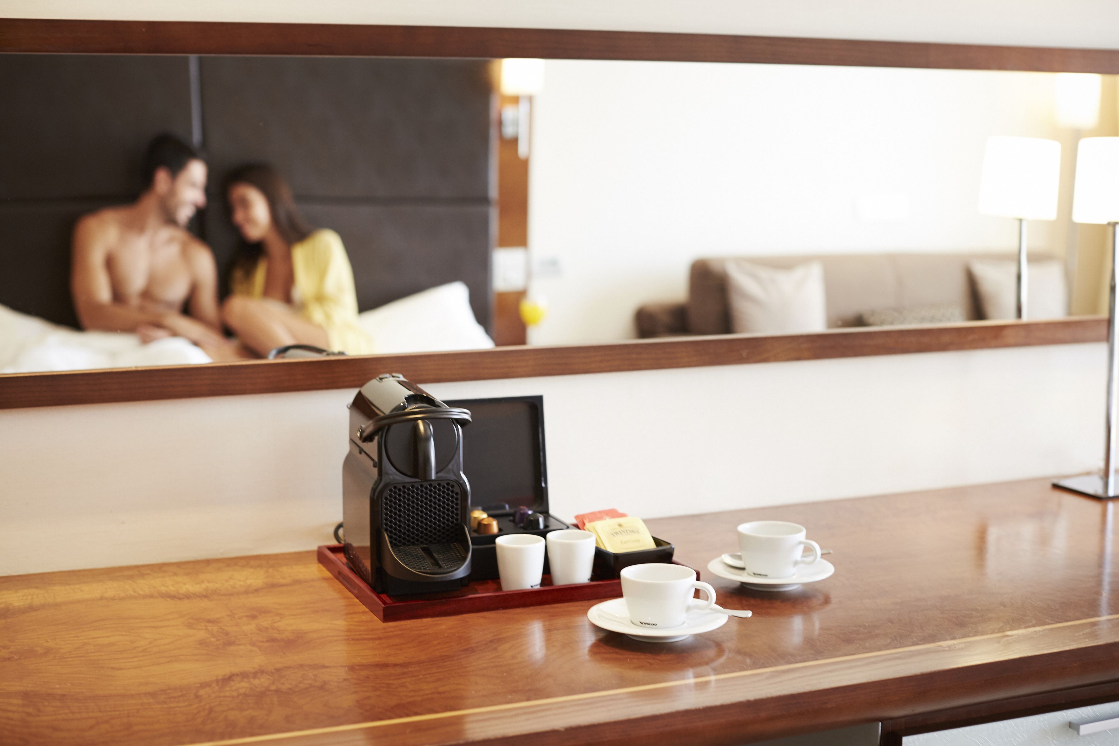 Una habitación de hotel con una mesita de noche de madera, una cafetera, tazas y una bandeja.