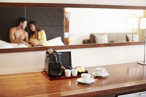 Una habitación de hotel con una mesita de noche de madera, una cafetera, tazas y una bandeja.