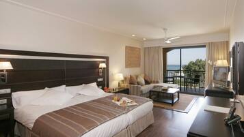 Habitación de hotel con una cama grande, un sofá, un escritorio y un balcón con vista al mar.