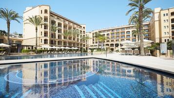 Un hotel con piscina, palmeras y tumbonas.