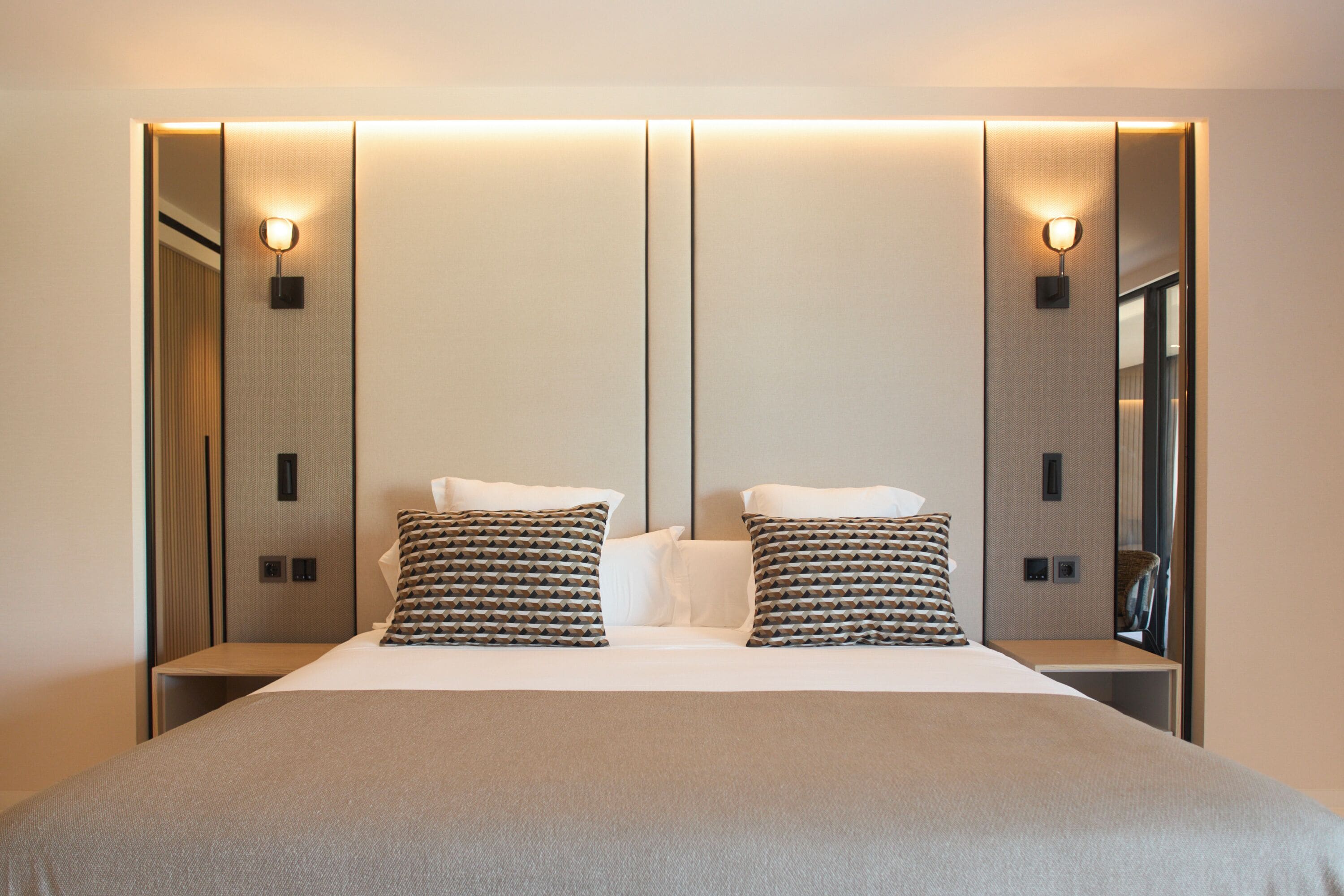 Une chambre d’hôtel moderne avec un grand lit, deux oreillers, une table de chevet et des lampes fixées au mur.