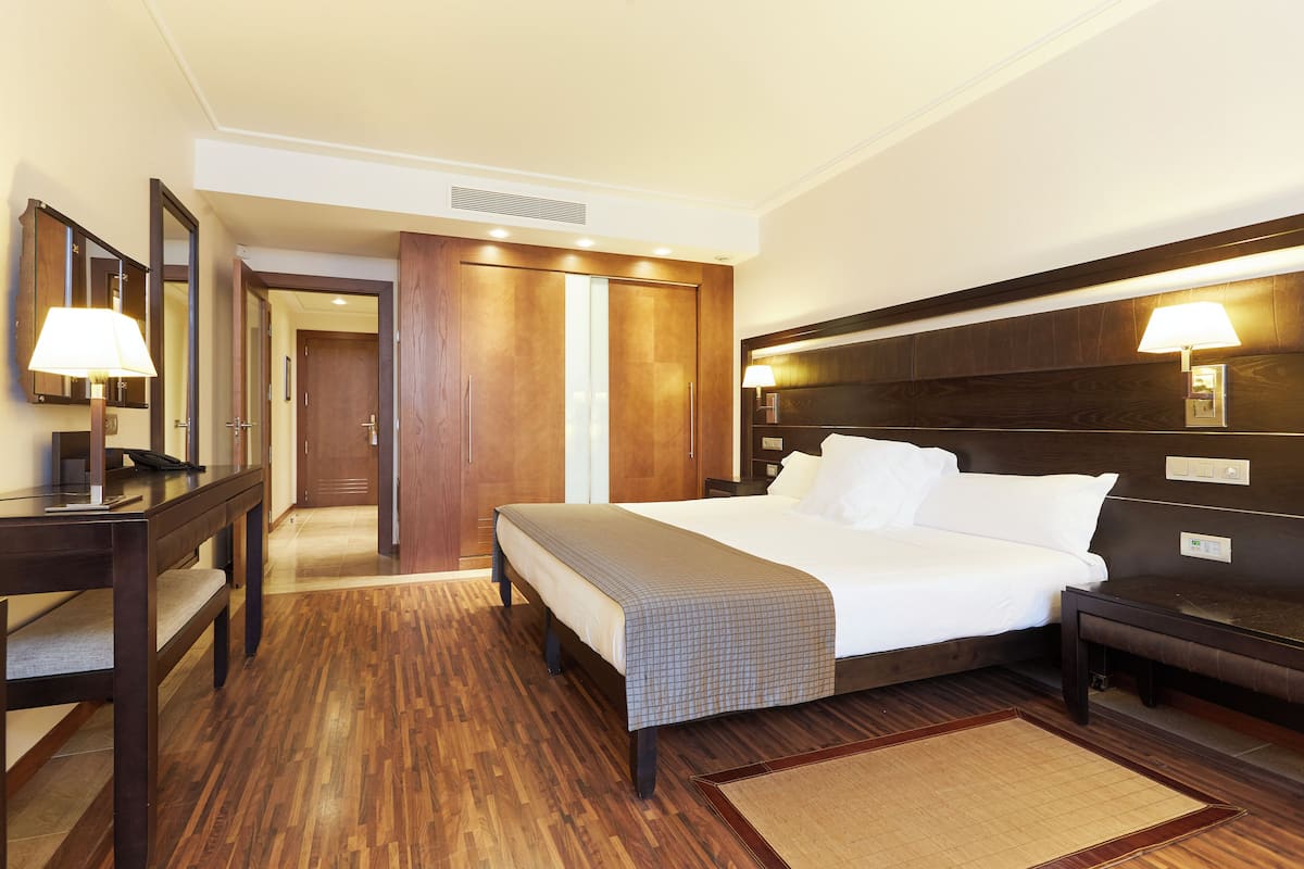 A hotel room with a bed, bedside tables, a desk, a mirror, a wardrobe, and a lamp.