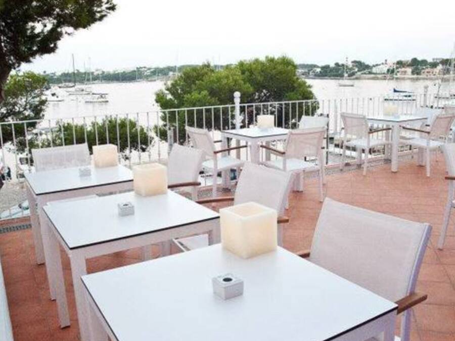 Un espace de restauration en plein air avec des tables et des chaises blanches, une vue sur l’eau et un grand luminaire sphérique blanc.