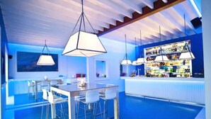 Zona de bar moderna con una decoración azul, con lámparas colgantes y una barra provista de diversas botellas.