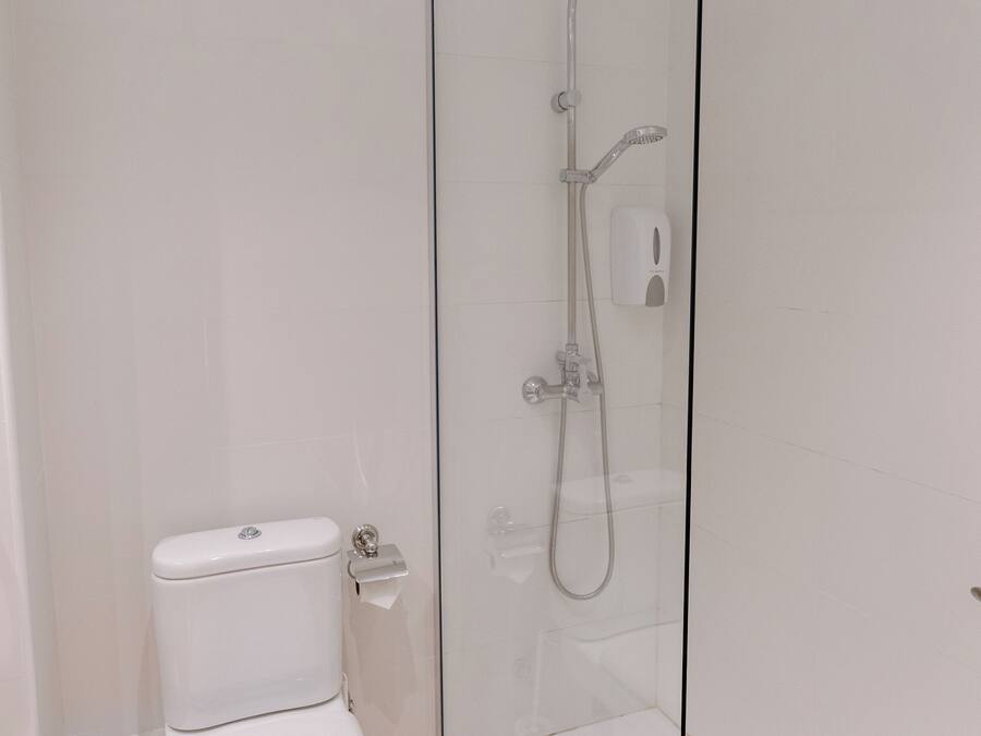 Un baño moderno con cabina de ducha de vidrio, inodoro blanco y suelo de baldosas.