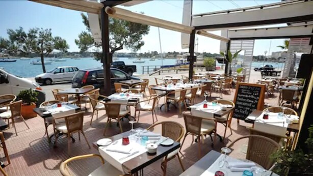 Un área de comedor al aire libre con mesas y sillas, con vistas a un puerto deportivo con barcos.
