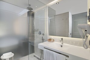 Un baño moderno con ducha envuelta en vidrio, lavamanos blanco y un secador de pelo fijado a la pared.