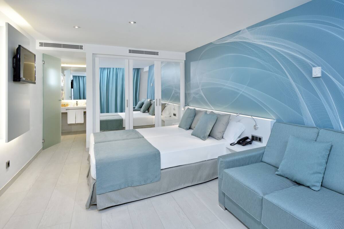 Une chambre d’hôtel moderne, équipée d’un lit, d’un canapé, d’un grand miroir et d’un mur orné de motifs bleus abstraits.