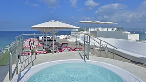 Zona de piscina con sillones de descanso y sombrillas en una terraza con vistas al mar.