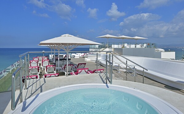 Zona de piscina con sillones de descanso y sombrillas en una terraza con vistas al mar.