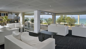 Una habitación de hotel moderna con muebles blancos, un muro de cristal y vista al mar.