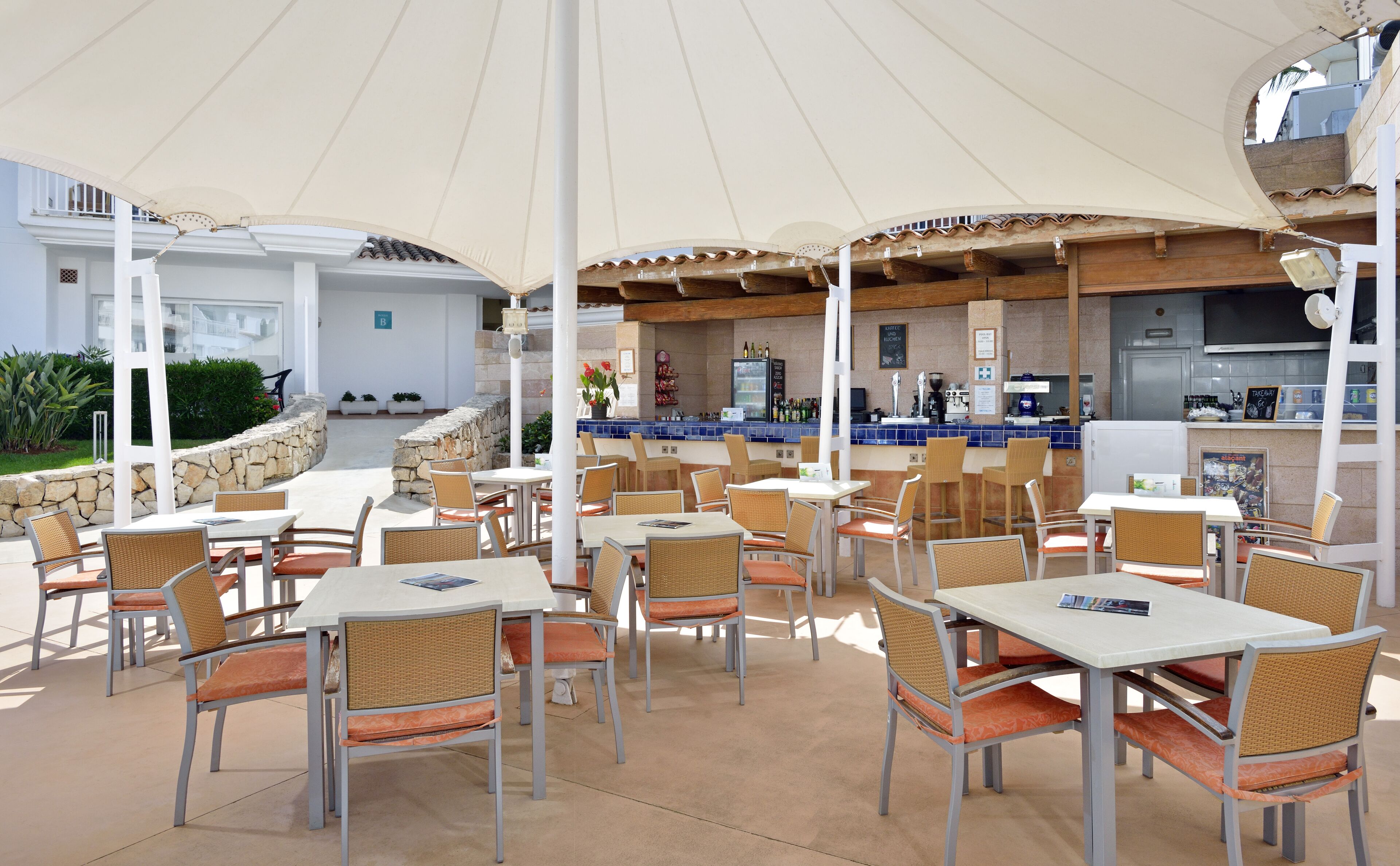 An outdoor patio area with tables and chairs, a bar, and a stone wall.