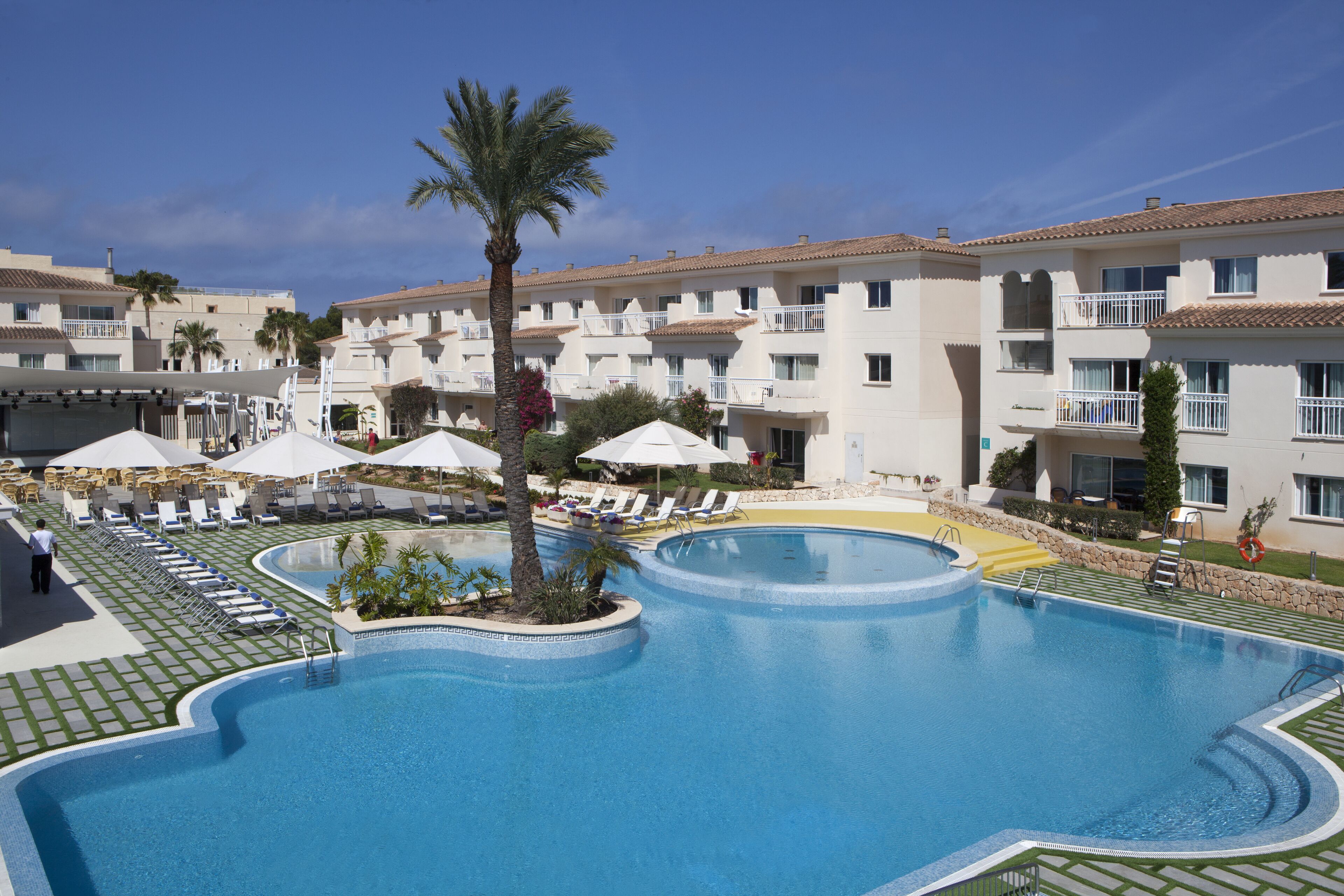 Un hôtel doté d’une grande piscine, de chaises longues et de palmiers.
