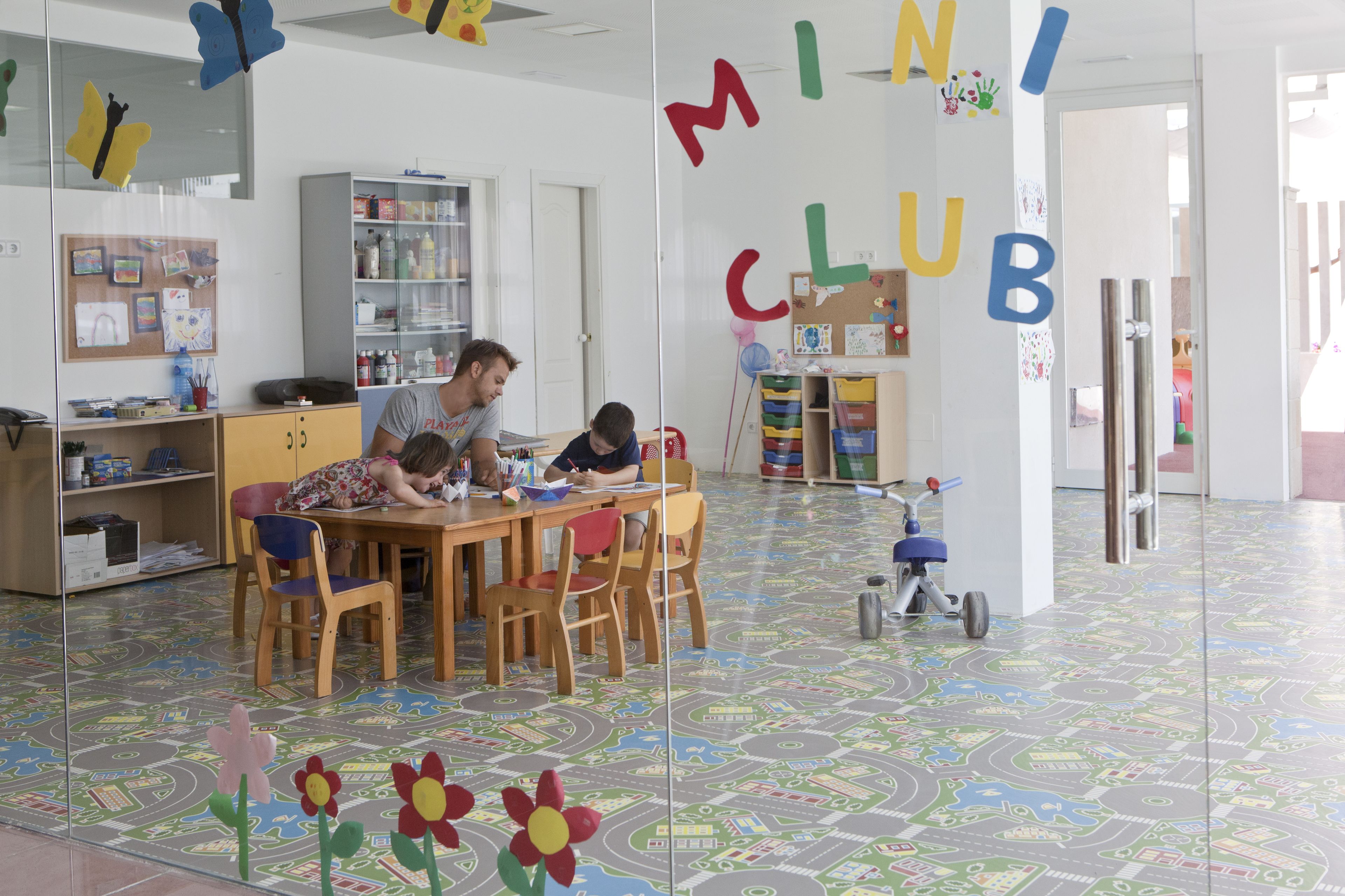 Uma sala de jogos infantil com piso colorido, uma mesa de madeira e cadeiras.