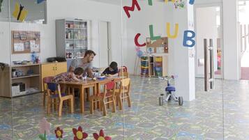 Uma sala de jogos infantil com piso colorido, uma mesa de madeira e cadeiras.