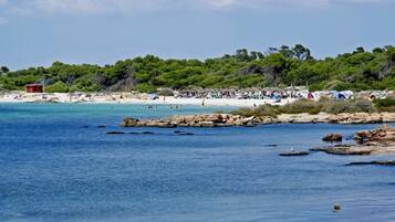 Una playa con agua azul cristalina, costa rocosa y una colina boscosa al fondo.