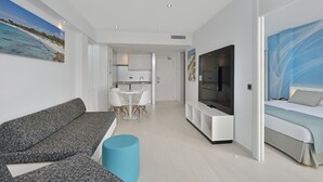 Una sala moderna con un sofá gris, un reposapiés azul, un televisor y una cama con colcha azul claro.