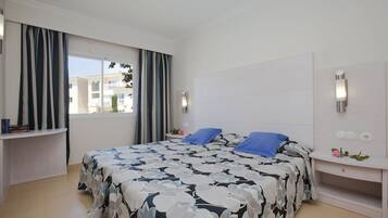 Un dormitorio con una cama grande, una mesita de noche, cortinas en la ventana y vistas a edificios.