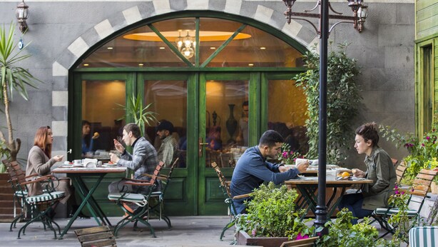 An outdoor cafe with tables and chairs, a green archway entrance, and potted plants. - Garden House Hotel - Special Class (Istanbul)