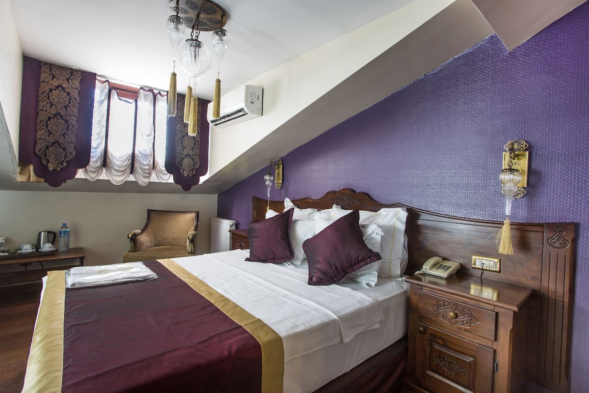 A hotel room with a large bed, a wooden nightstand, a chair, and a desk with a lamp.