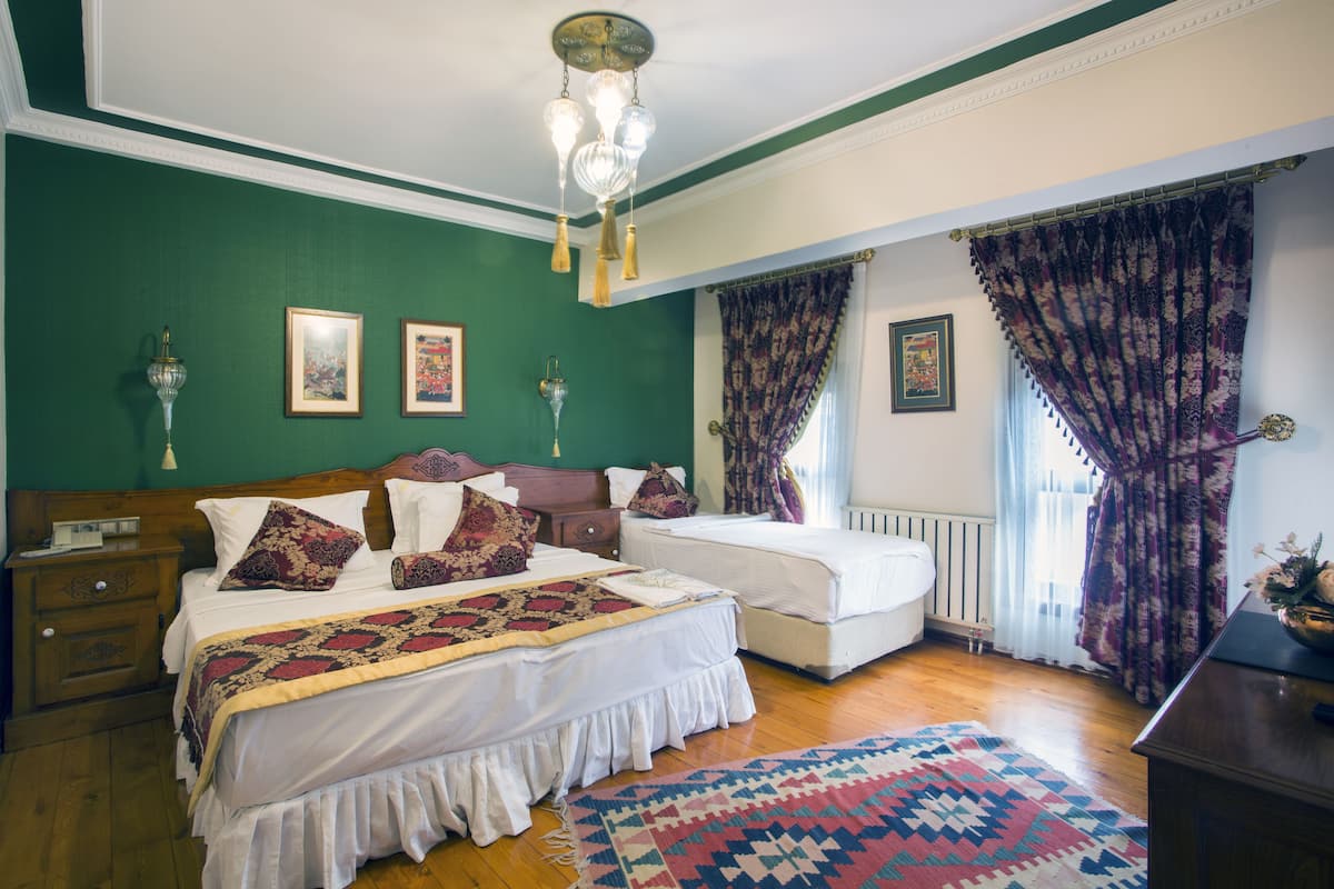 A bedroom with two beds, a wooden floor, green walls, and a patterned rug.