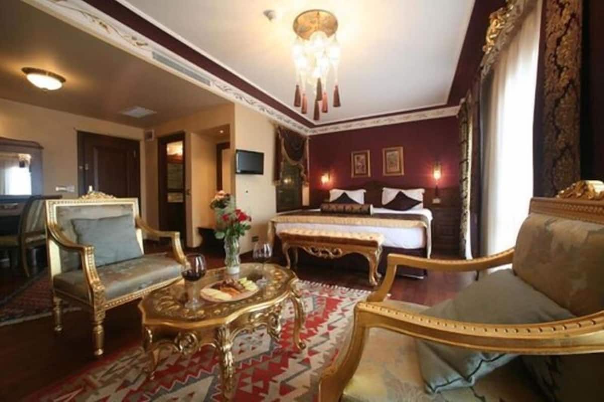 A hotel room with a large bed, two ornate armchairs, a small table with a vase, and a patterned carpet.
