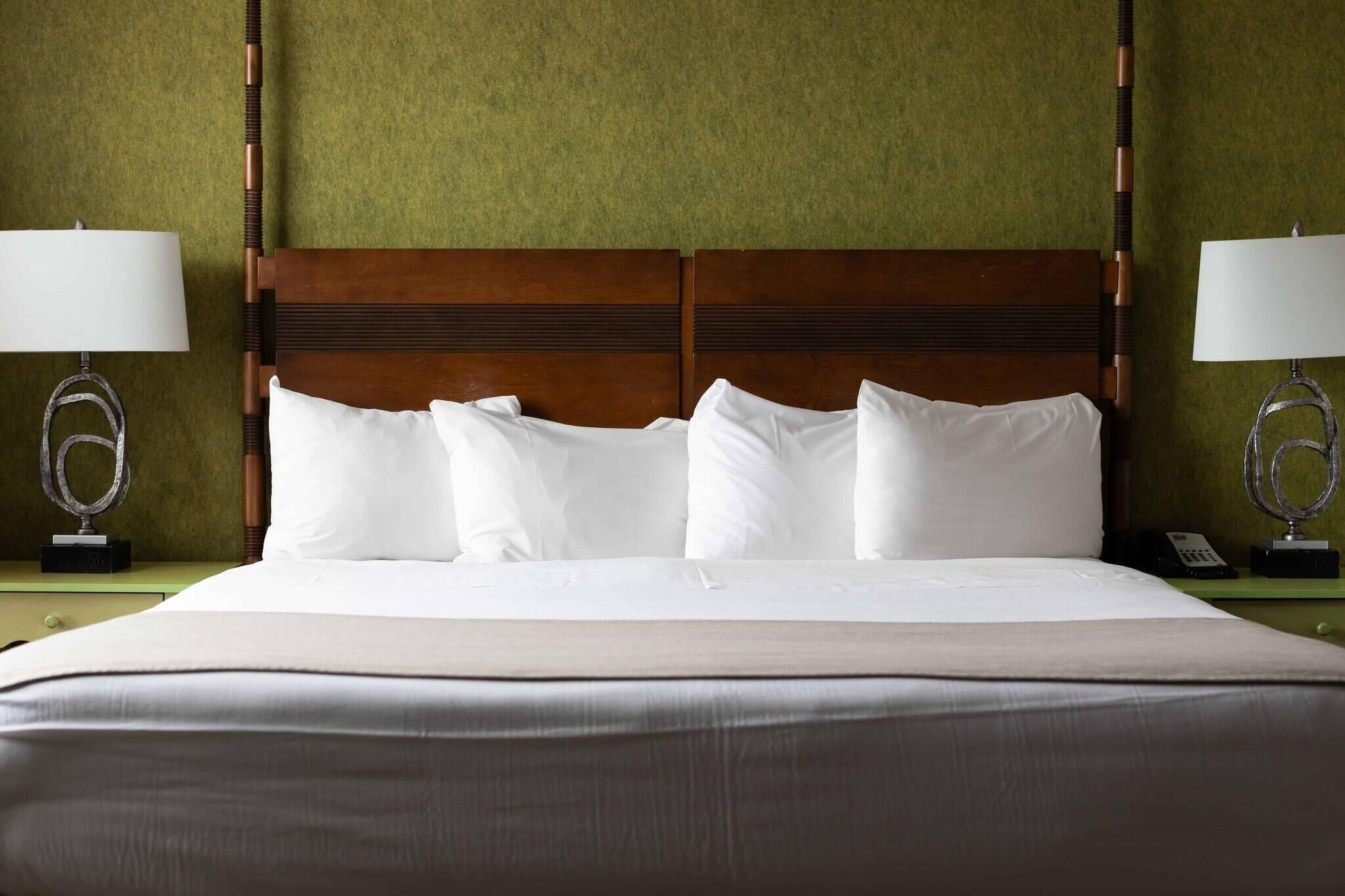 Una cama bien tendida con sábanas blancas, cabecera de madera y dos lámparas de noche con base circular.