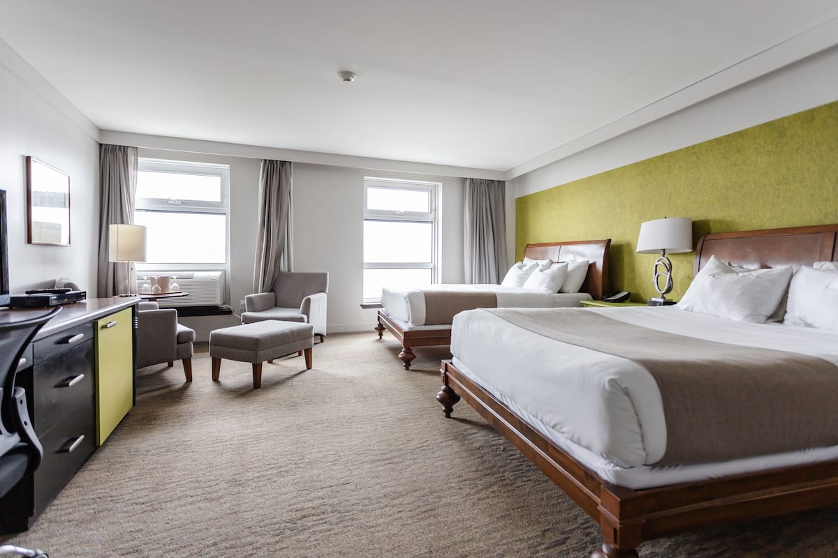 Una habitación de hotel con una cama grande, dos sillones, un escritorio con una computadora y una pared de acento verde.