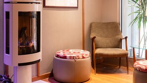 A modern room with a wood-burning stove, a framed picture on the wall, a comfortable chair, and a potted plant by the window. - Hôtel Champlain Vieux Québec (Québec City)