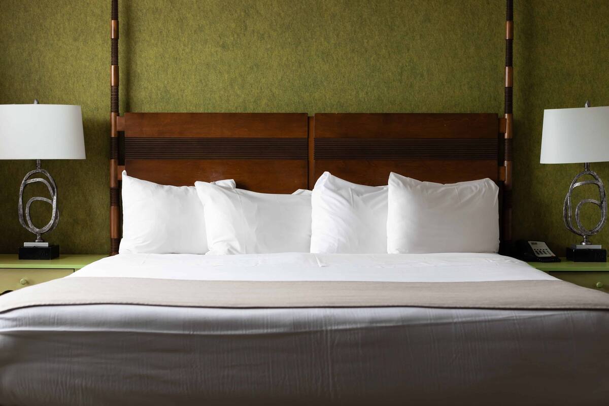 Una cama bien tendida con sábanas blancas y cabecera de madera en una habitación de hotel.