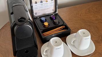 Una máquina de café Nespresso, una caja de cápsulas y dos tazas blancas sobre una mesa de madera.
