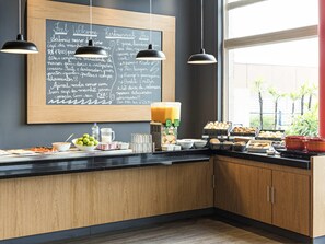 A breakfast buffet with a chalkboard menu, a fruit juice dispenser, and various breakfast items. - ibis Tamboré (Barueri)