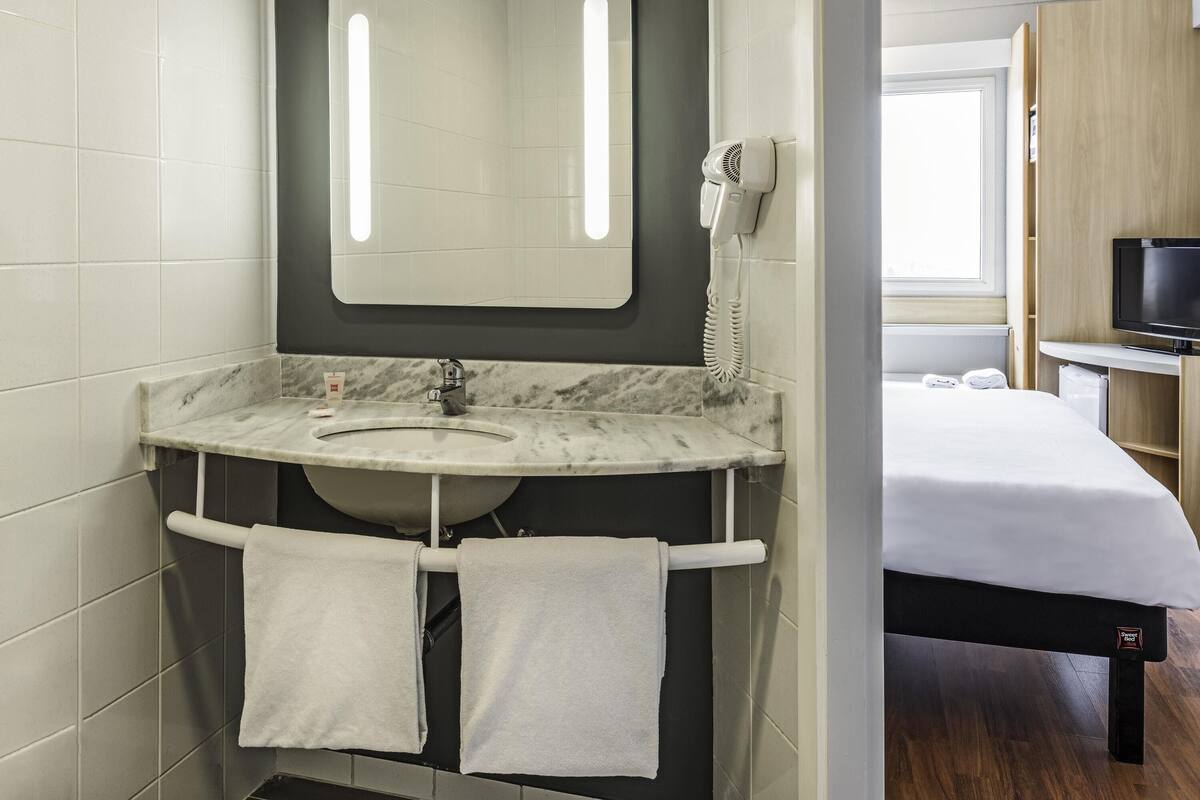 A bathroom with a marble sink, a hairdryer, a mirror, and a towel rack.