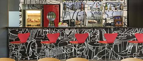 A bar area with a black and white mural, red chairs, and a variety of bottles on shelves.