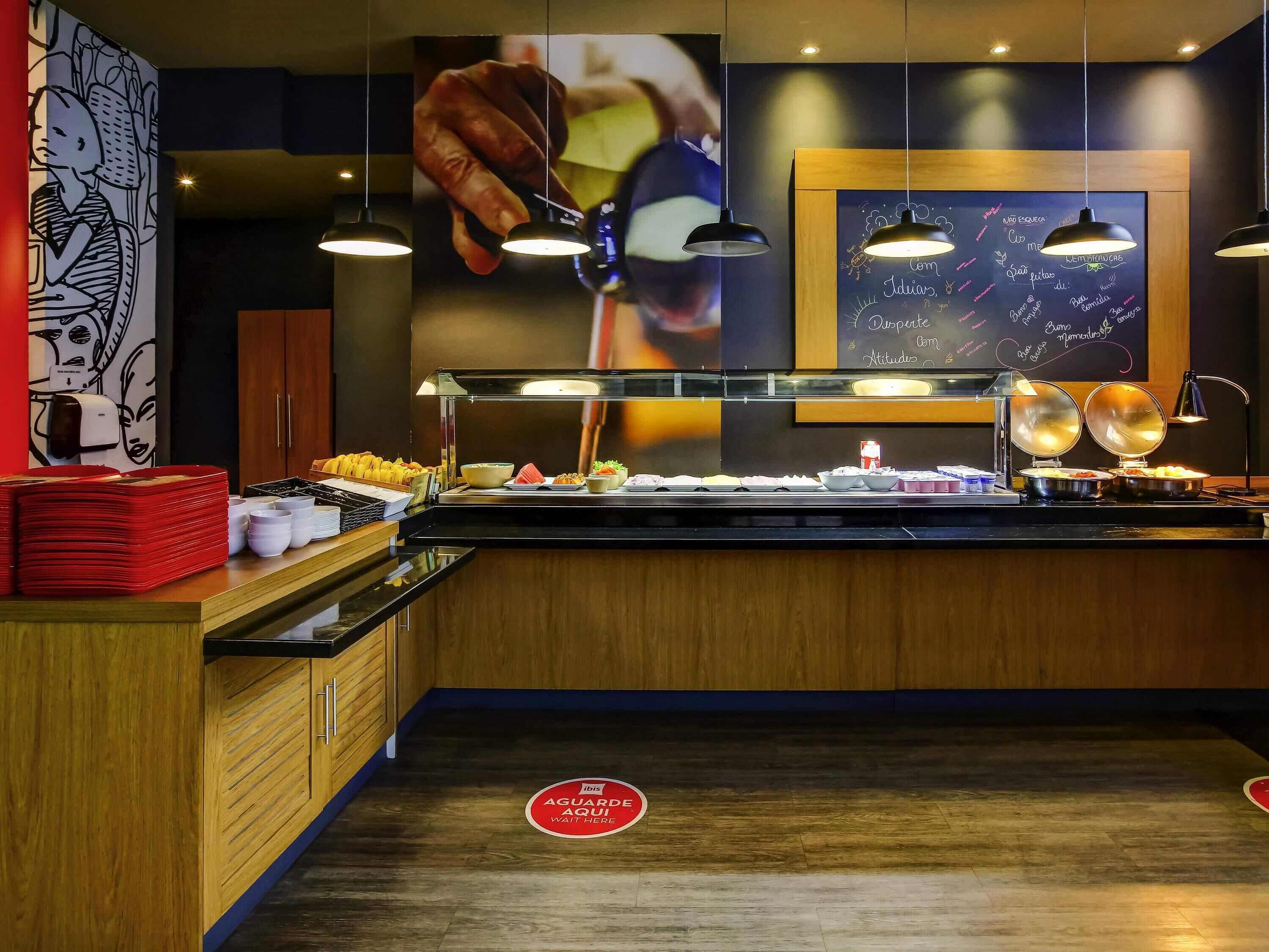 A buffet area with a variety of food items, a chalkboard with menu writing, and a sign indicating a waiting area.