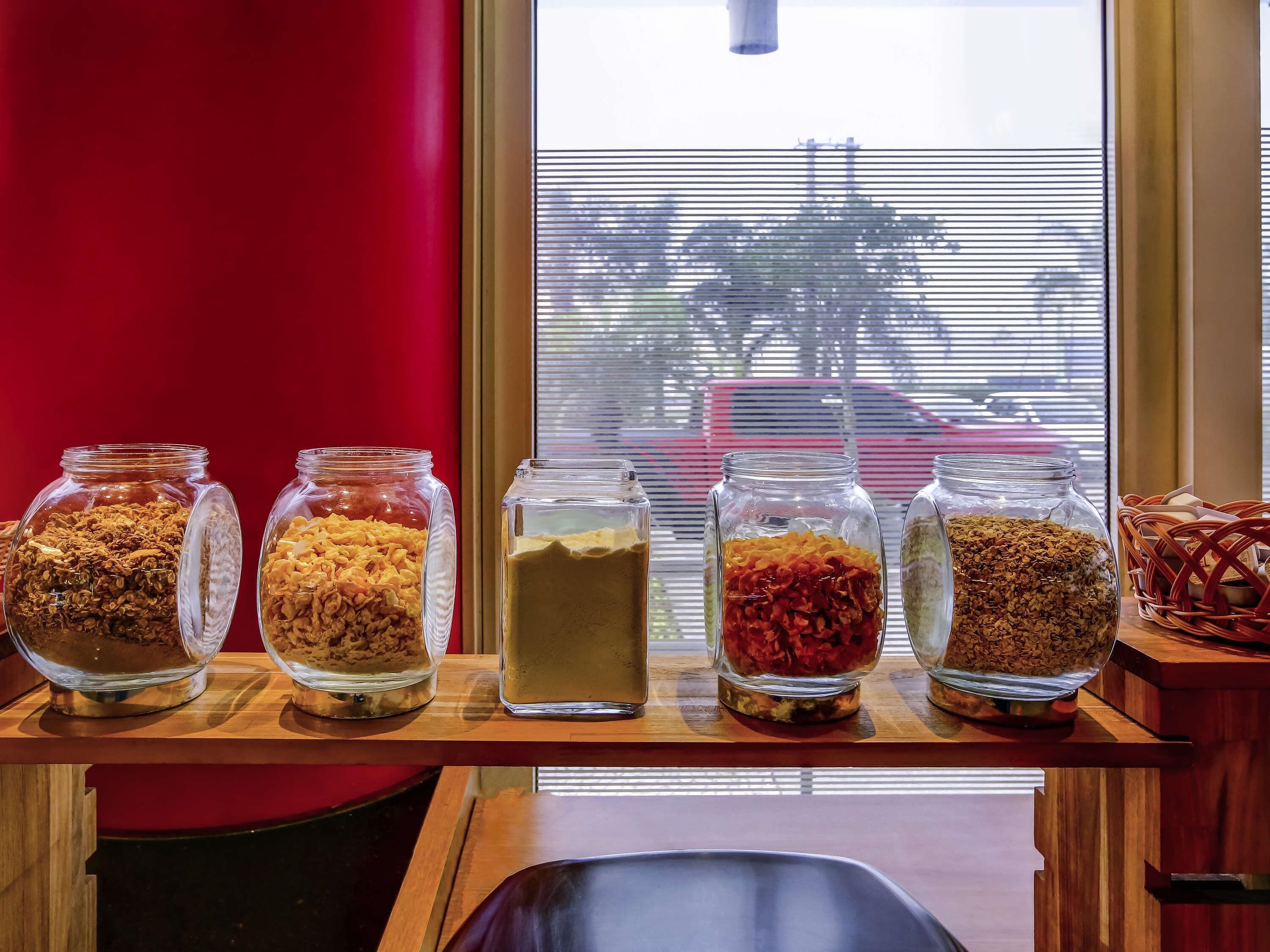 A wooden shelf with five glass jars containing various food items.