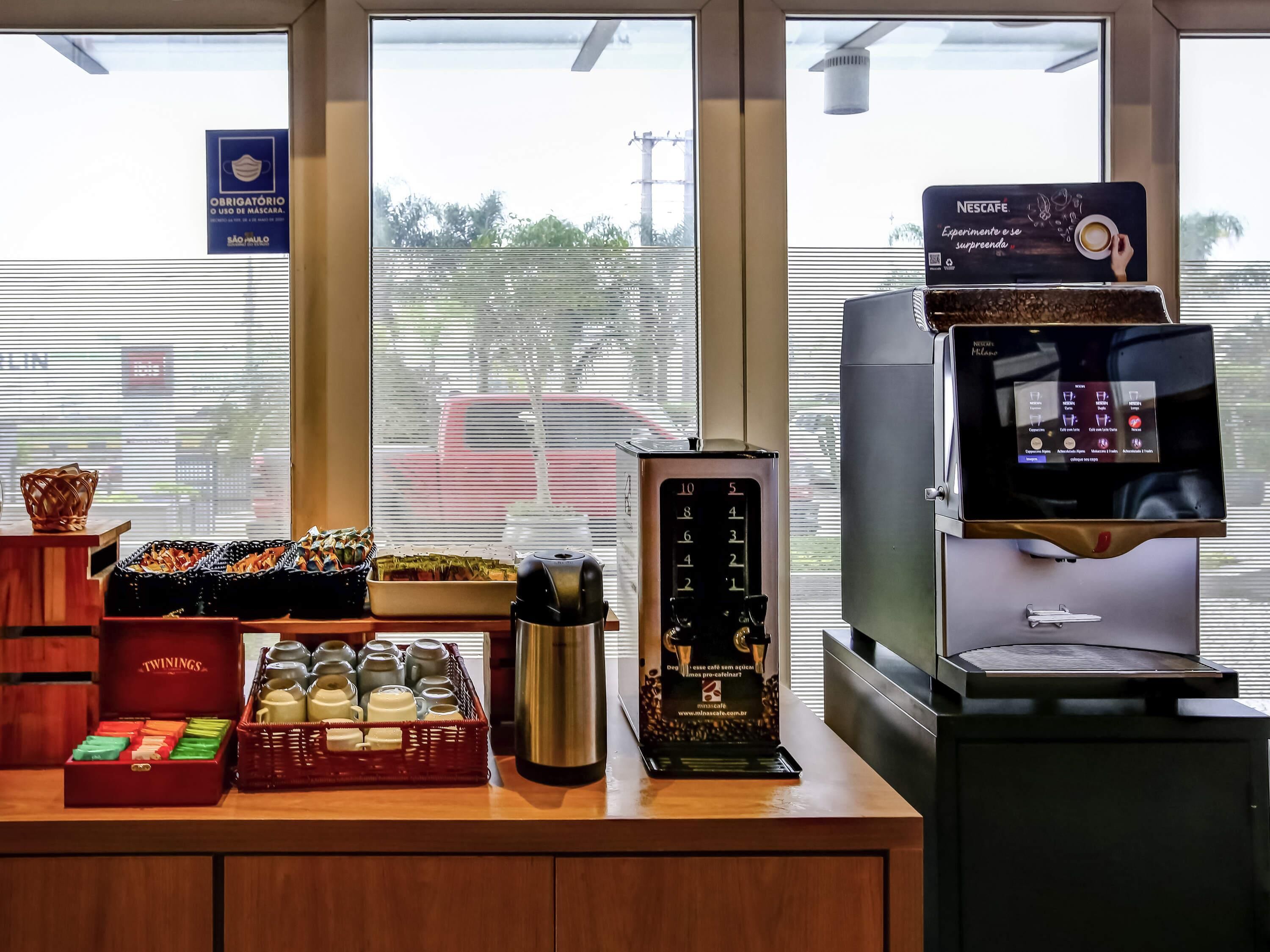 A coffee station with a Nescafé machine, a thermos, and a variety of coffee beans and mugs.