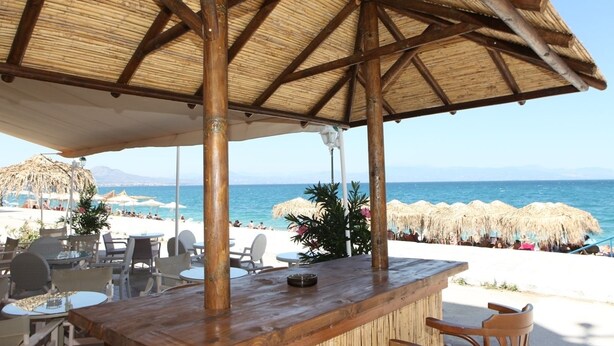 A beachside bar with a thatched roof, outdoor seating, and a view of the sea. - Mantas Seaside Boutique Hotel (Loutraki-Agioi Theodoroi)