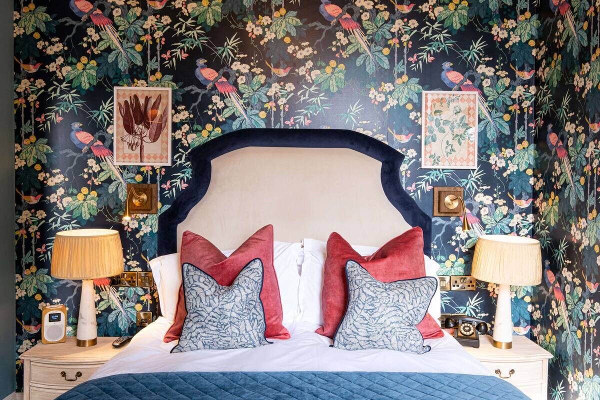 A bed with a dark headboard, two bedside lamps, and a floral wallpaper.
