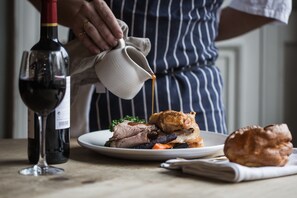 A person pouring sauce over a dish with meat and vegetables. - The Park Hotel (Teddington)