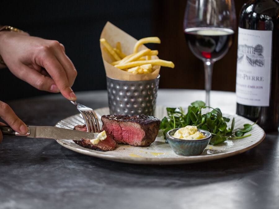 A steak with fries and a glass of red wine on a plate.