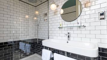 A bathroom with a white sink, black tiled walls, a glass shower enclosure, and a mirror above the sink.
