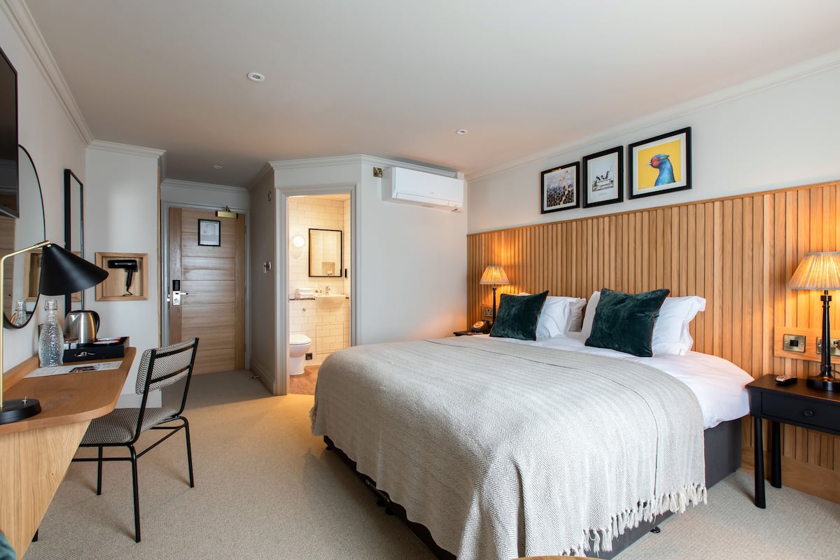 A hotel room with a bed, desk, chair, and a bathroom visible through an open door.