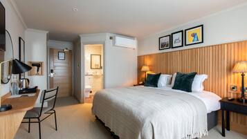 Habitación de hotel con cama, escritorio, silla y baño visible a través de una puerta abierta.