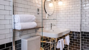 A modern bathroom with white subway tiles, a glass shower enclosure, a white sink with chrome fixtures, and two white towels on a shelf.